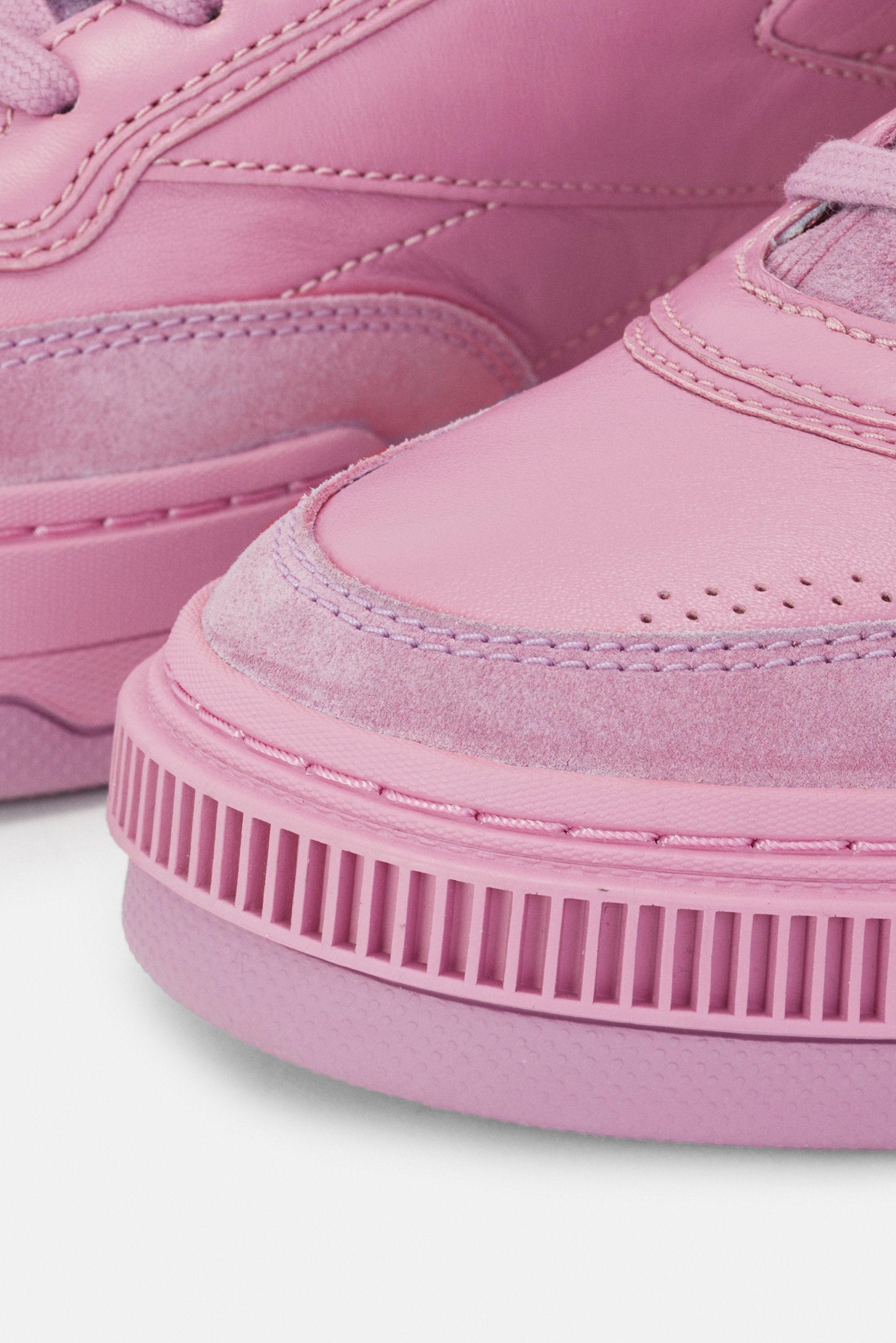 Close-up of pink sneakers, featuring textured suede and smooth leather, with a thick ridged sole and detailed stitching.