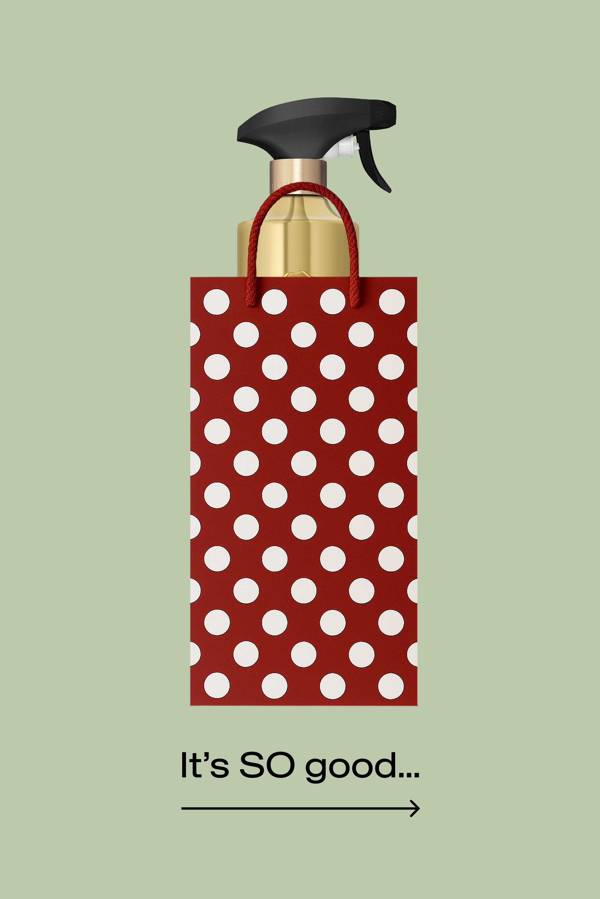 Spruzzatore dorato in una borsa rossa con grandi pois bianchi e manici rossi su sfondo verde chiaro.