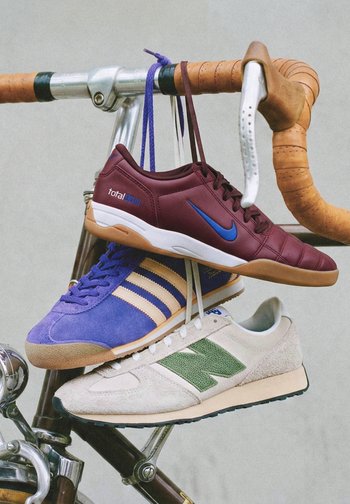Tres zapatillas deportivas de diferentes marcas colgadas por los cordones del manillar de cuero marrón de una bicicleta vintage.
