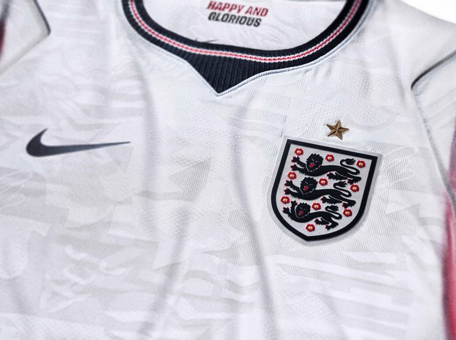 Weißes englisches Fußballtrikot mit schwarzem Nike-Logo, Drei-Löwen-Wappen mit roten Rosen und dem Motto „Happy and Glorious“ im Innenkragen.