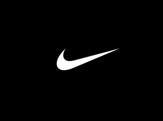 Biały logo Nike w kształcie pioruna na czarnym tle. Logo ma gładki, zakrzywiony kształt z ostrym końcem, co nadaje mu dynamiczny wygląd.