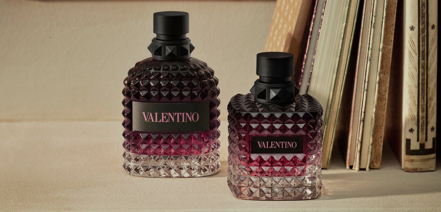 Twee met studs versierde glazen Valentino parfumflesjes met een roze verloopvloeistof staan op een beige oppervlak naast op een rijtje geplaatste boeken.