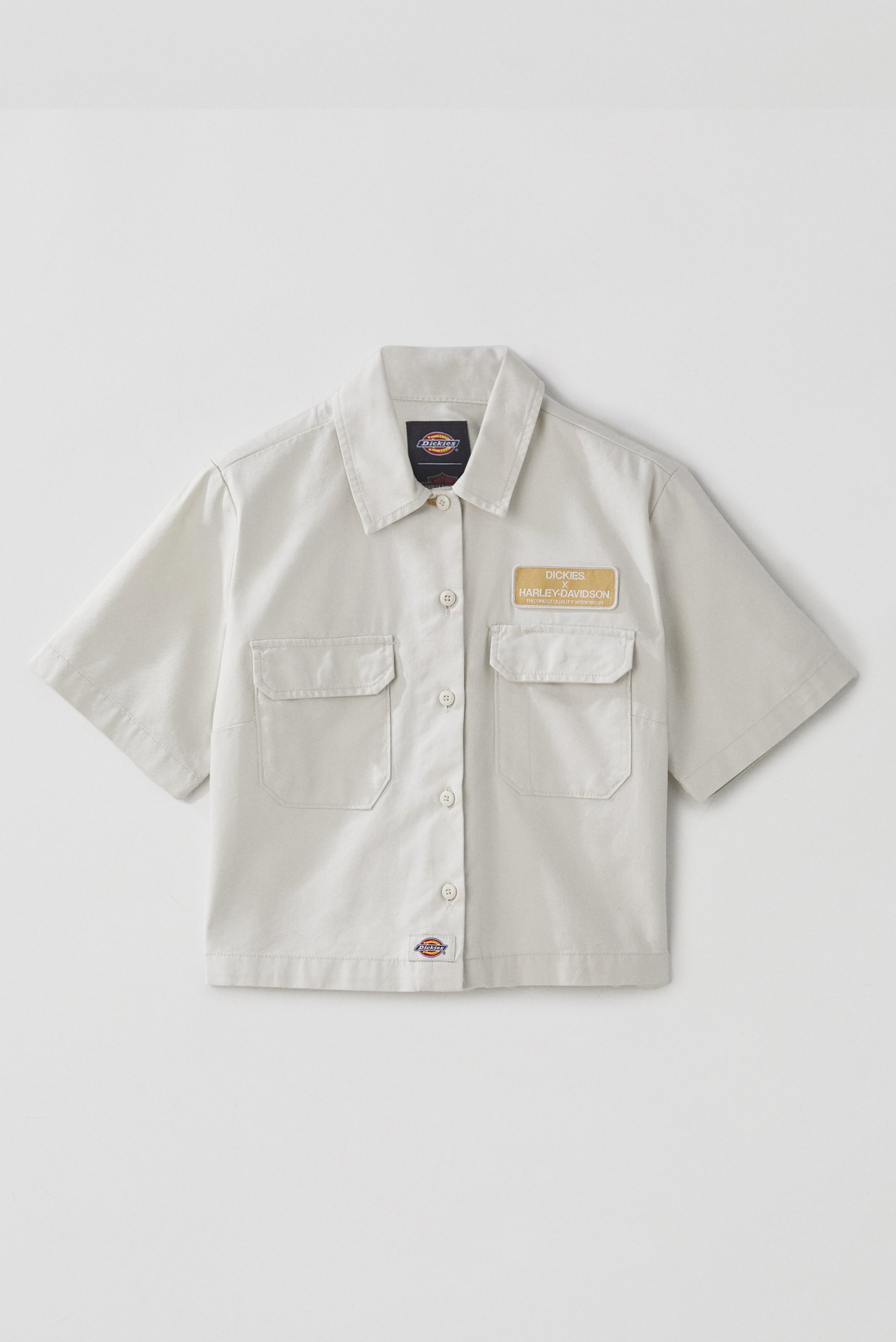 Lichtbeige kortekoolshirt met een kraag, voorzien van twee borstzakken en een logovlag met de tekst "Dickies. Harley-Davidson."
