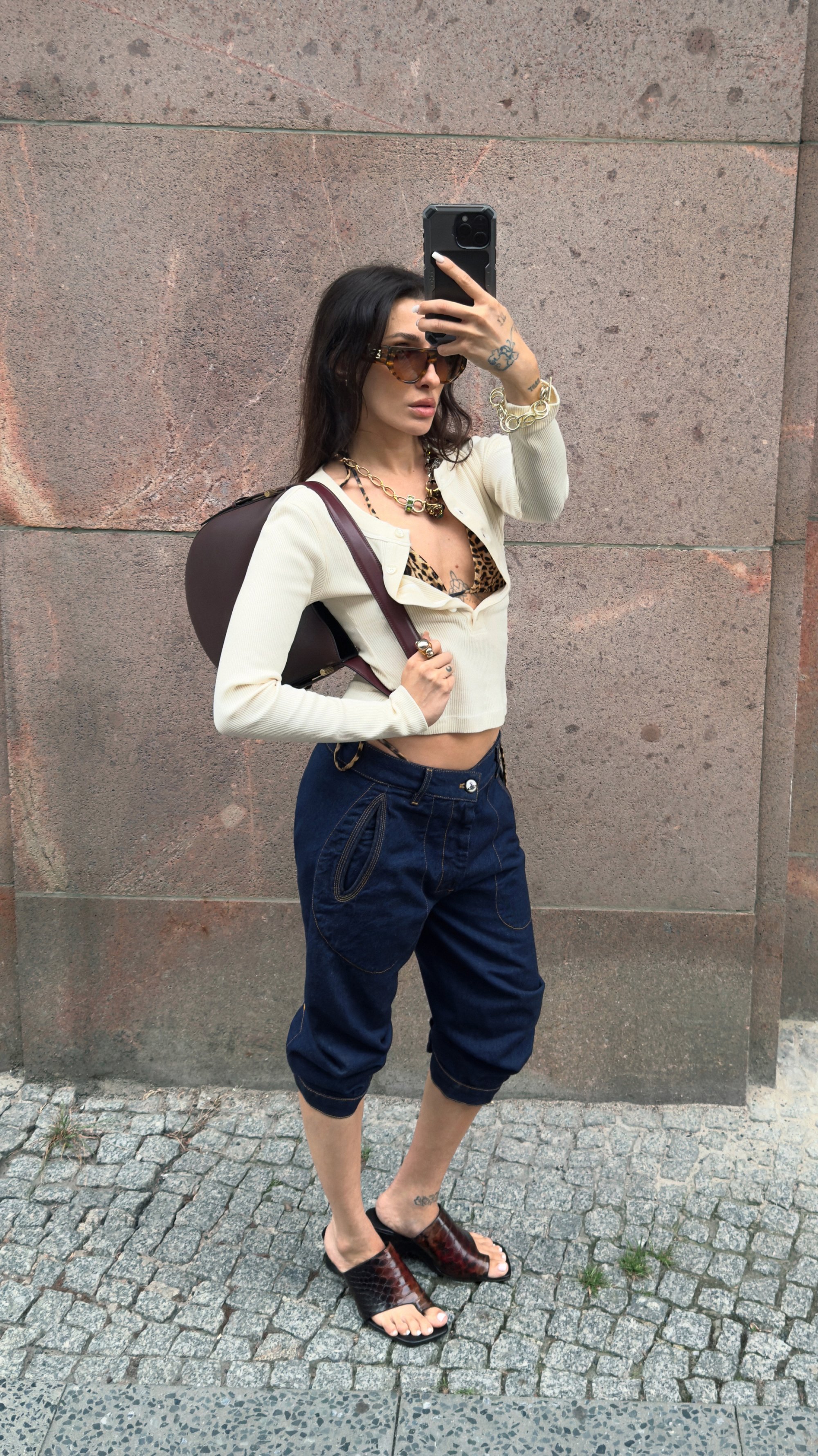 Top corto a coste bianco, bralette con stampa leopardata, pantaloni ampi blu scuro con tasche uniche, zaino marrone e sandali scuri.