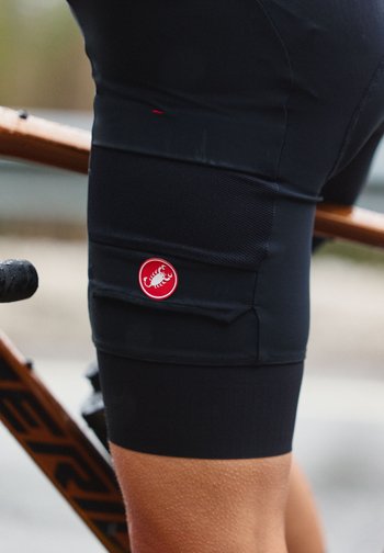 Syklist iført svarte polstrede shorts med rød skorpionlogo, sittende på en brun sykkelramme.