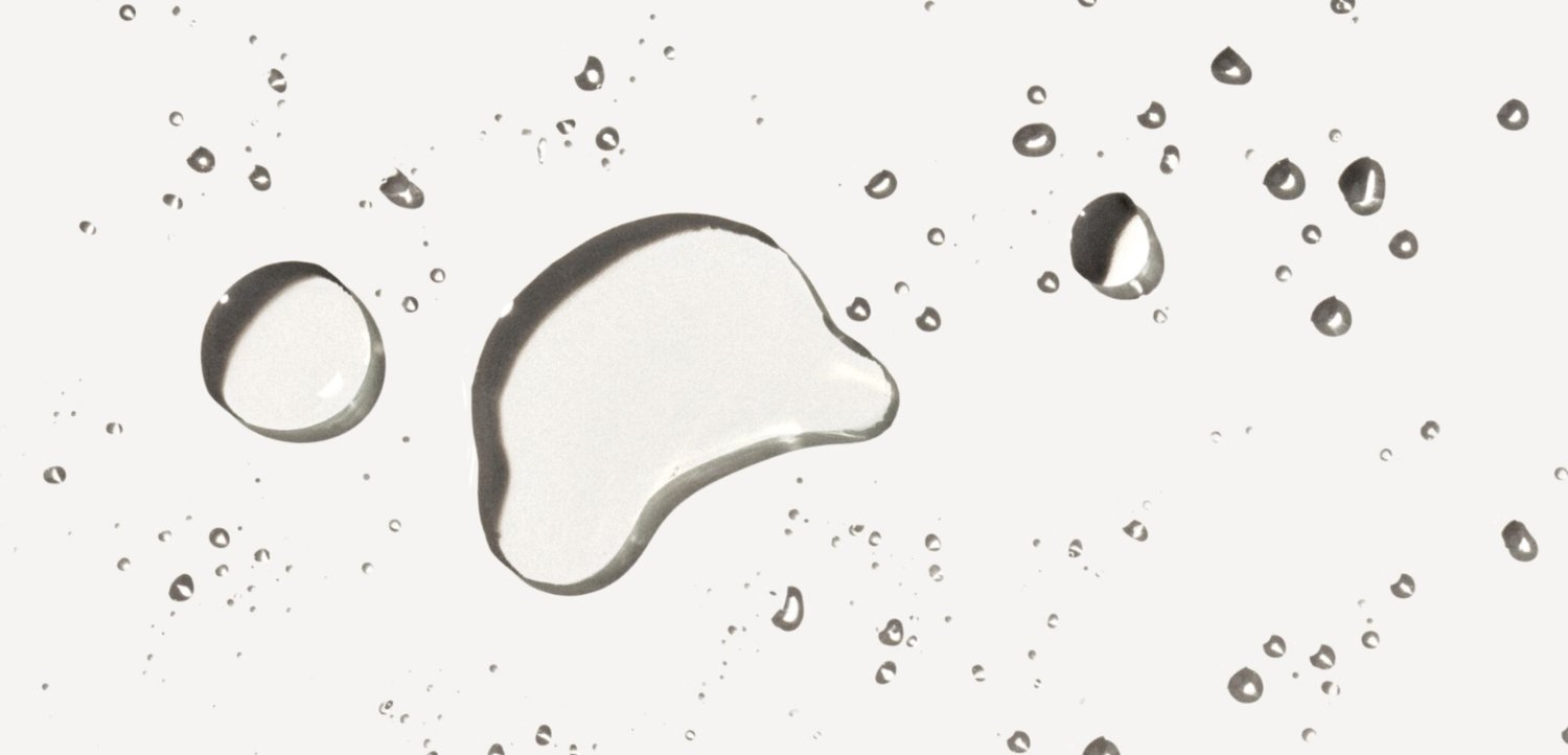 Varias tamaños de gotas de agua claras dispersas sobre una superficie lisa y de color claro con sombras suaves.