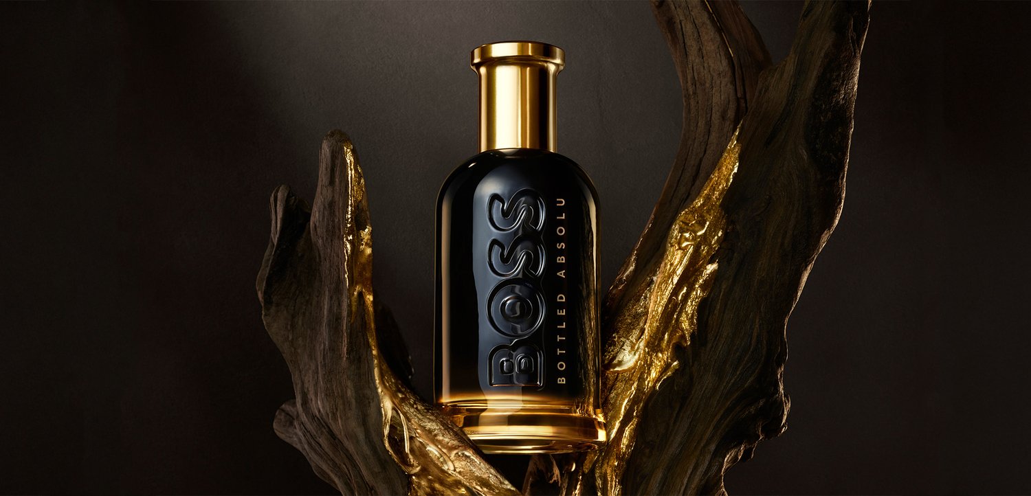 Schwarze und goldene BOSS Bottled Absolu Parfümflasche auf strukturiertem dunklem Holz mit goldenen Akzenten vor dunklem Hintergrund.