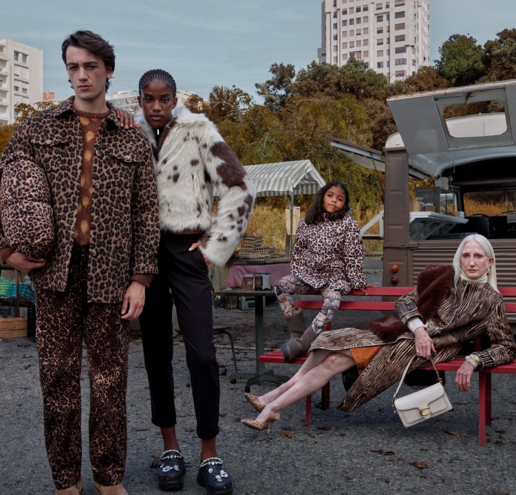 Four models don outfits featuring animal prints: a brown leopard coat, a white faux fur jacket, and a mix of patterns. The backdrop includes a food truck.