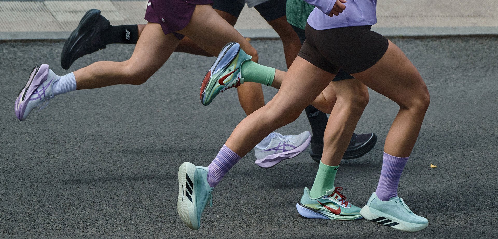 Three runners mid-stride on a road wearing athletic shoes and shorts in a street running event.