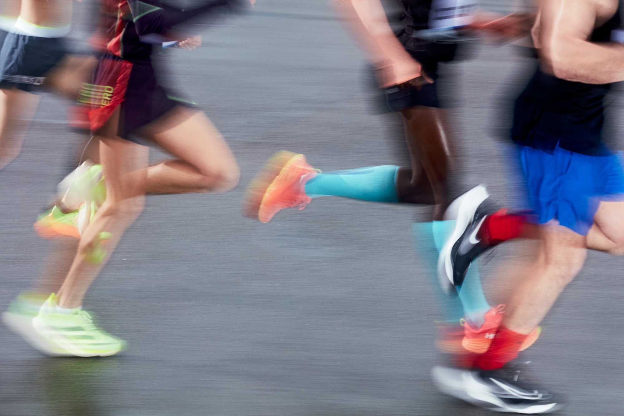 Runners in action with blurred motion, showcasing diverse footwear and athletic attire on a track, conveying energy and speed.