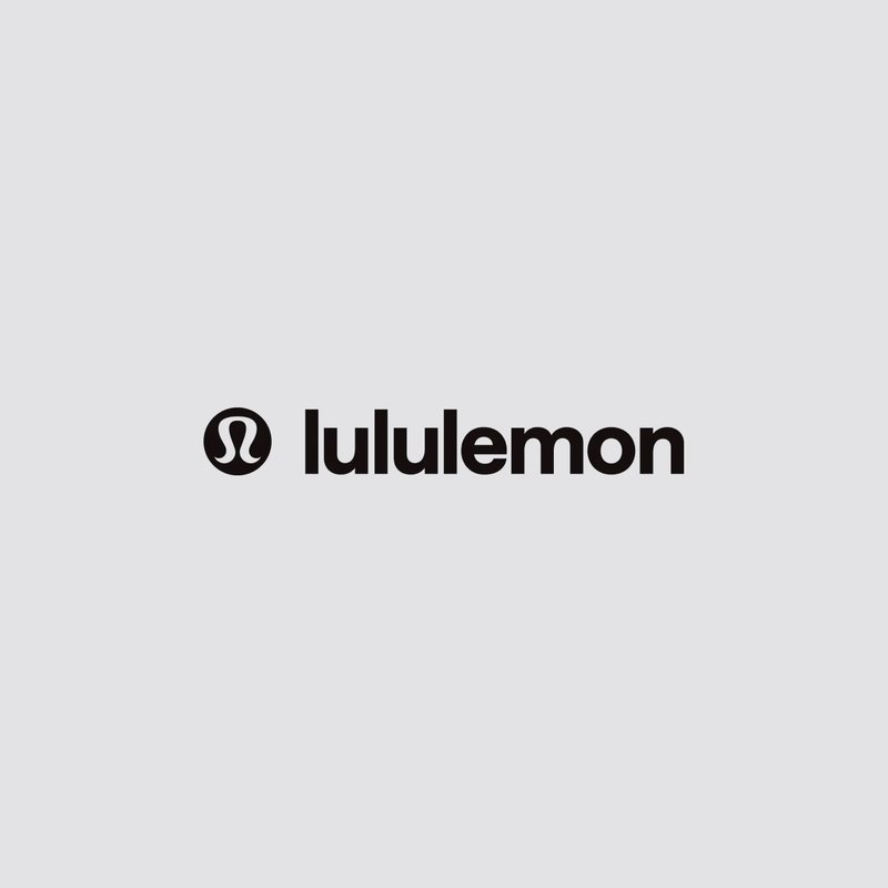 Zwart tekenslogo van "lululemon" in vetgedrukte kleine letters op een lichtgrijze achtergrond. Het ontwerp bevat een cirkelvormig embleem.