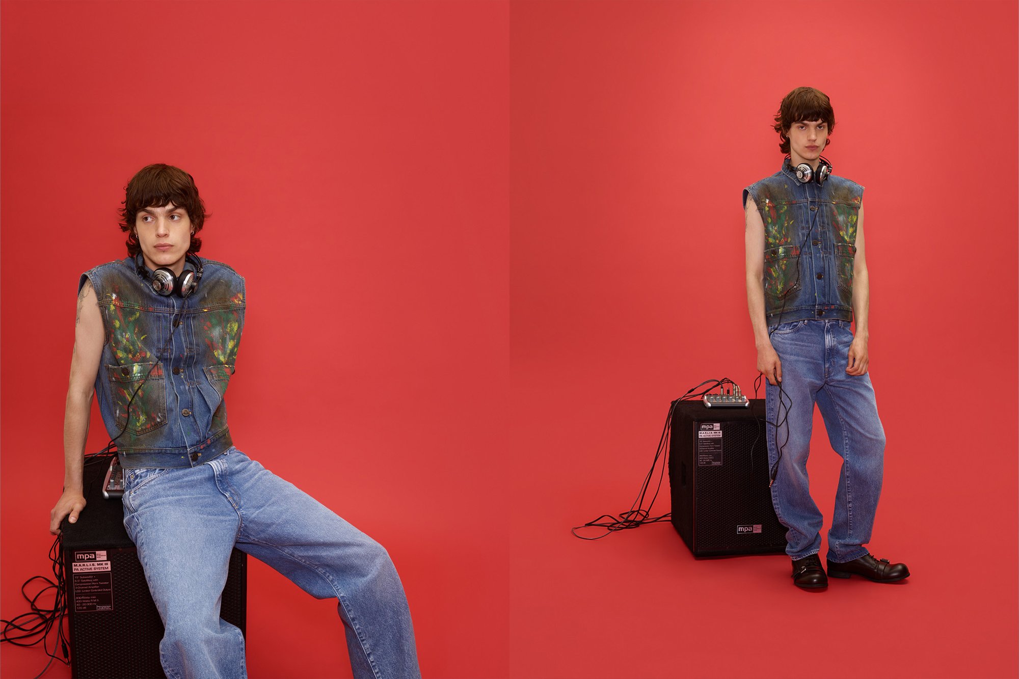 Persona joven con auriculares, vistiendo un chaleco de mezclilla pintado y jeans, posando sentado y de pie junto a un altavoz negro contra un fondo rojo.