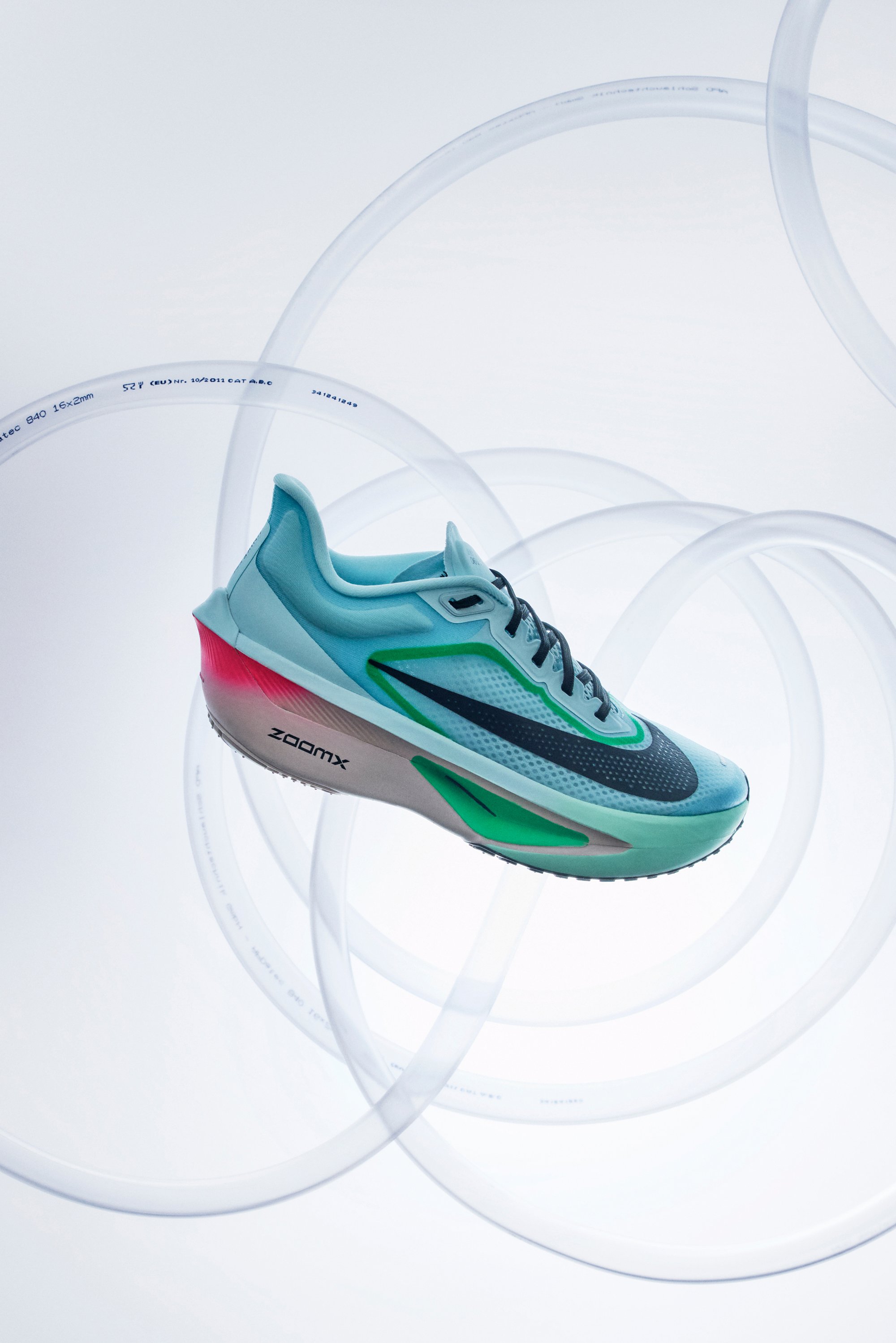 Svetlo modrá atletická obuv s okrovými a ružovými akcentmi, sieťovina na vrchu a čierny Swoosh logo. Disponuje hrubou podrážkou s označením "ZOOMX".