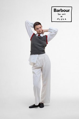 Model poses with hands behind head, dressed in a grey sweater vest over a white shirt and white trousers, set against a minimalist background.