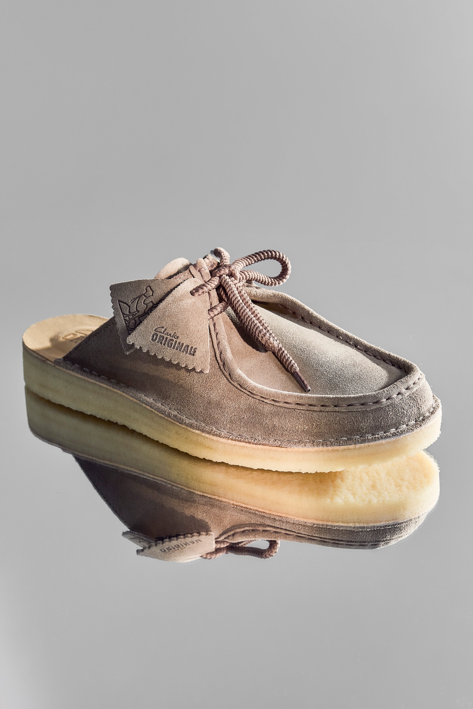 Brown suede shoe with a rounded toe and front lacing, resting on a reflective surface, displaying the "Clark Originals" logo.