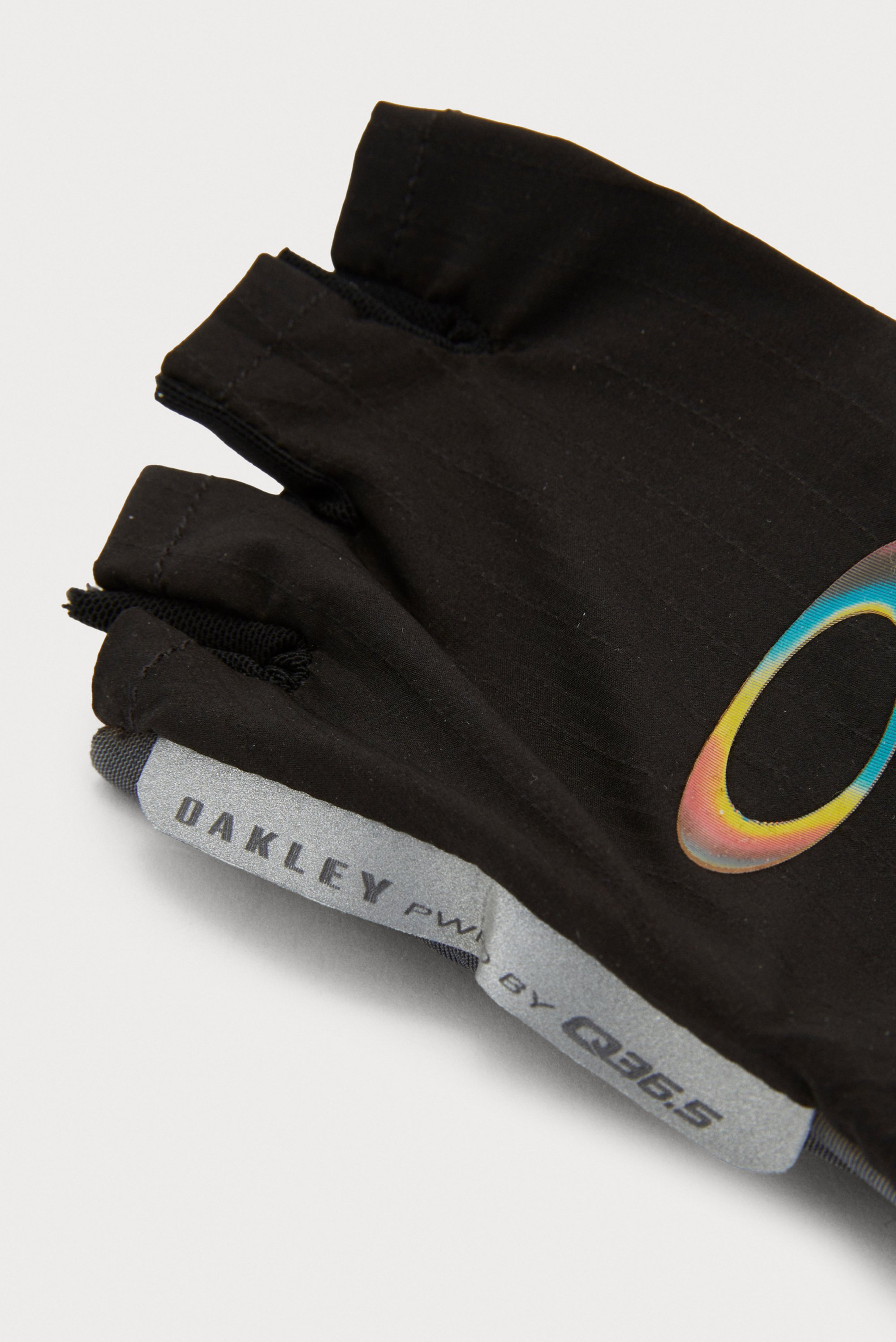 Black cycling gloves with an open-finger design feature the Oakley logo and a colorful gradient "O" on the palm side.