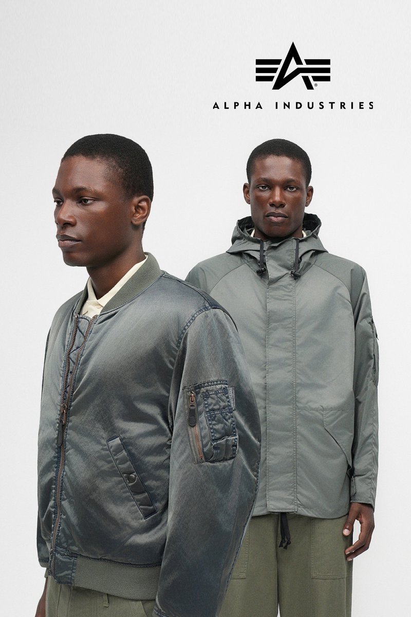 Twee mannen in grijze bomber- en hoodie-jassen, staand tegen een effen witte achtergrond met het Alpha Industries-logo.