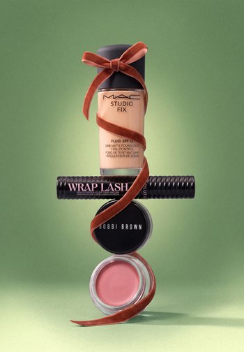 Le fond de teint MAC Studio Fix, le mascara Wrap Lash et le blush Bobbi Brown sont empilés sur un fond vert, enveloppés d'un ruban couleur rouille.