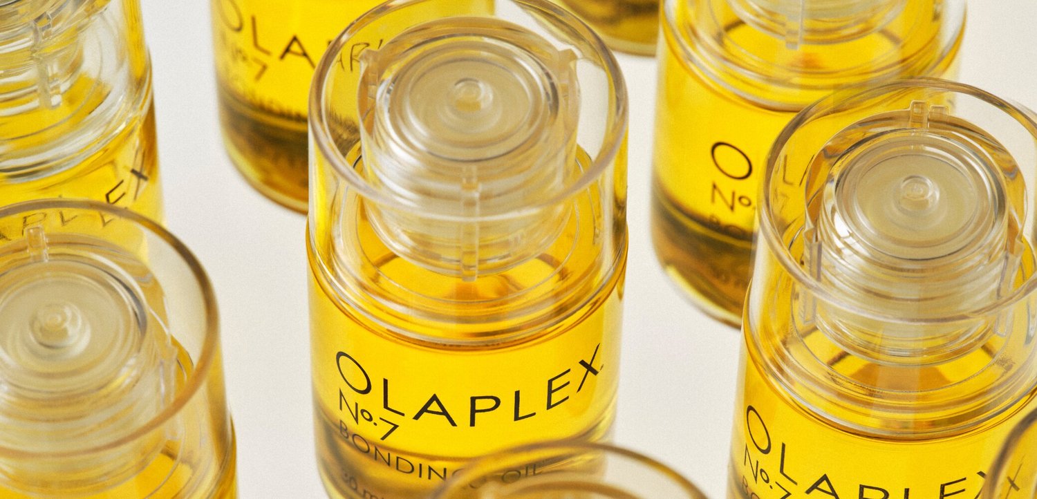 Kilka przezroczystych butelek Olaplex No. 7 Bonding Oil z żółtym płynem w środku, ułożonych na białej powierzchni.
