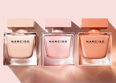 Tres elegantes frascos de perfume en diferentes tonalidades de rosa, etiquetados como "Narciso", dispuestos sobre un suave fondo rosa.