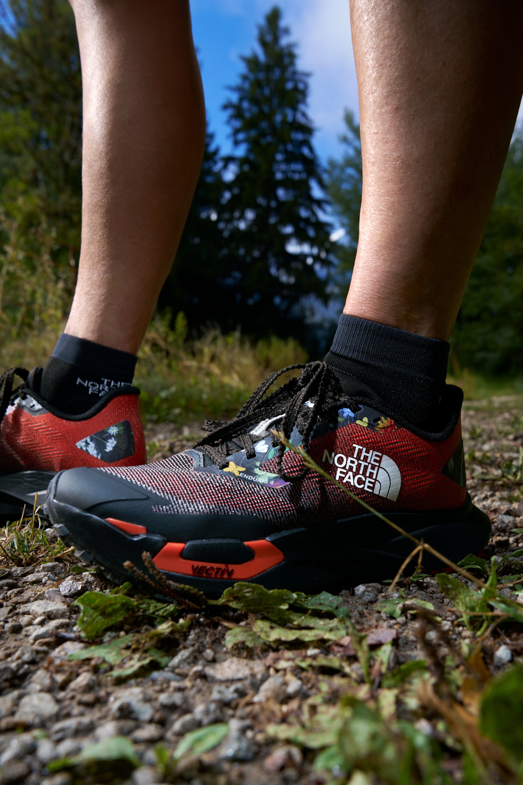 Red and black trail running shoes featuring a mesh upper, black laces, and a white logo. They are designed with a rugged sole and vibrant accents.