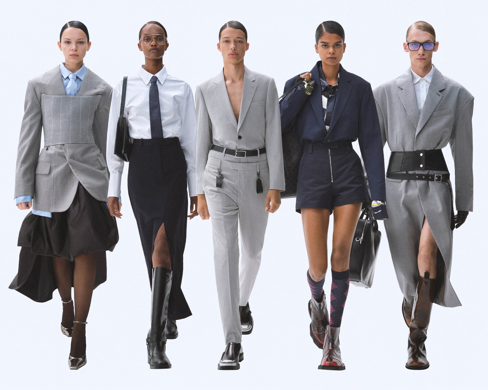 Cinco modelos muestran una variedad de trajes de alta moda, que incluyen blazers ajustados, faldas y botas, todo con un fondo neutral.