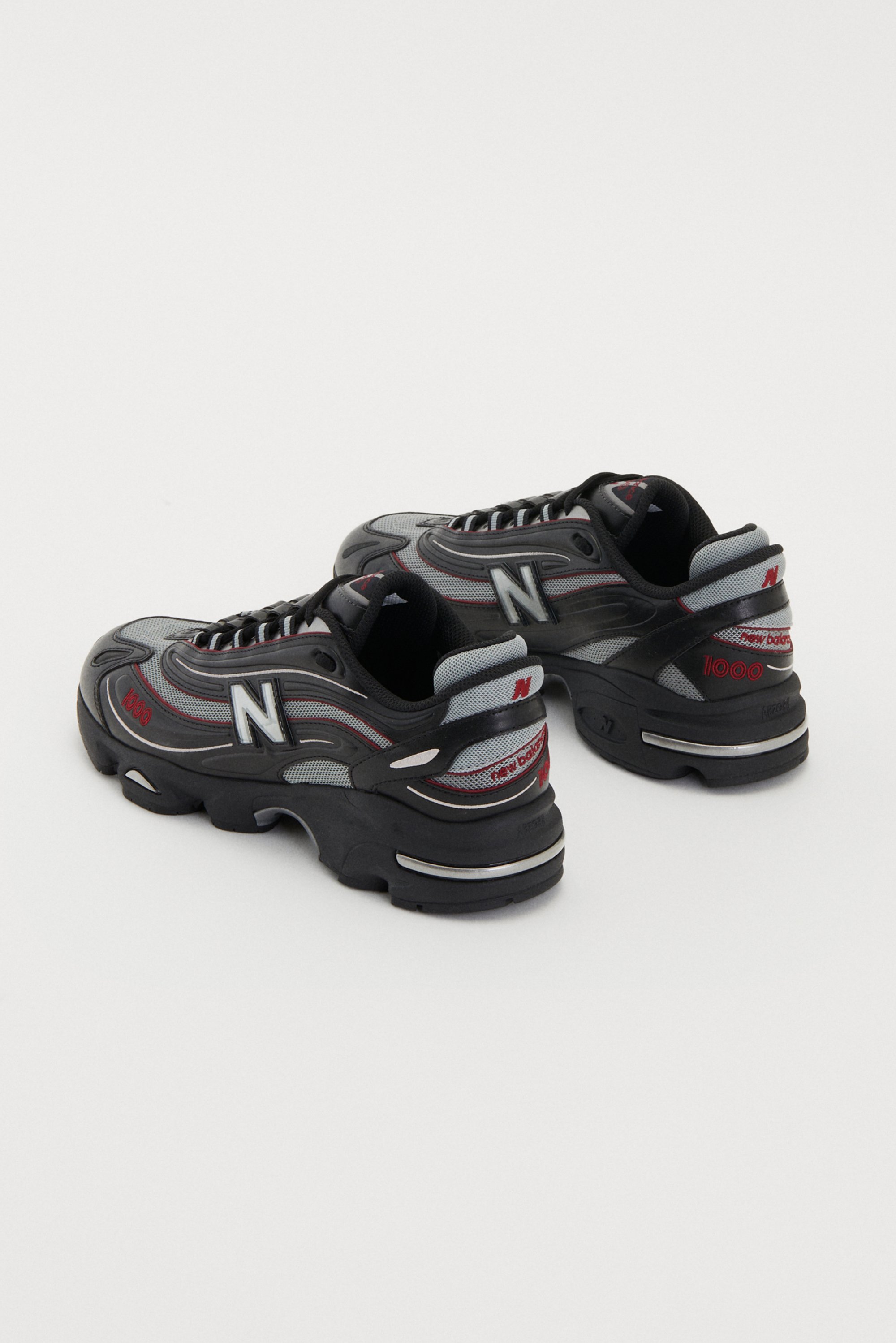 Black and gray New Balance sneakers with a chunky sole, featuring red accents and the brand's logo on the side and heel.