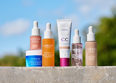 Seis productos de cuidado de la piel Lumene están dispuestos sobre una superficie de piedra con un fondo natural desenfocado. Los artículos incluyen sueros y cremas en envases coloridos.
