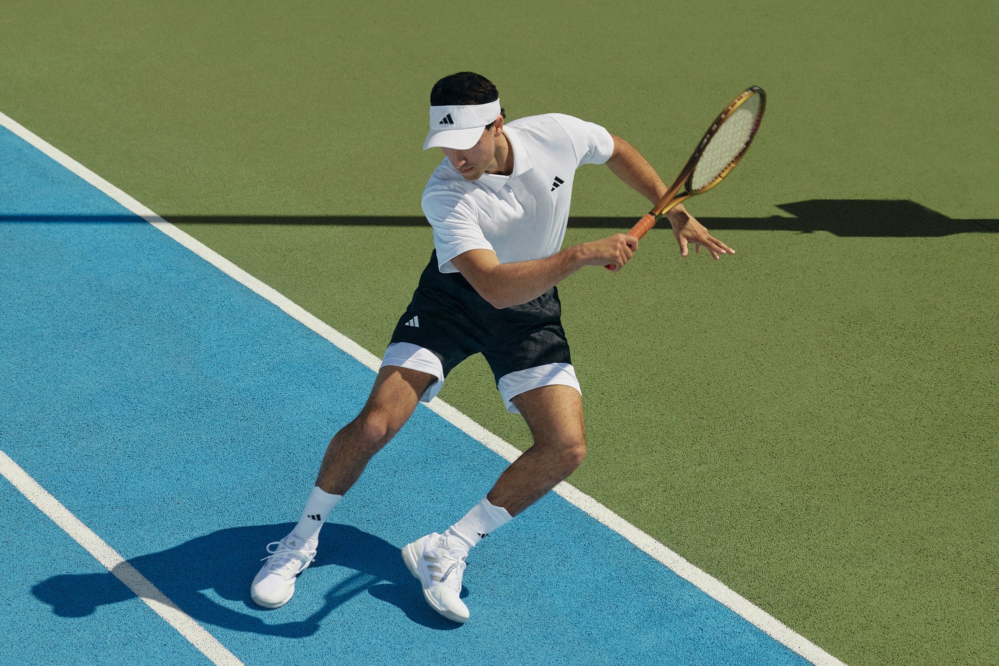 A man in a white athletic shirt and black shorts prepares to hit a tennis ball on a blue and green court, holding a racquet in motion.