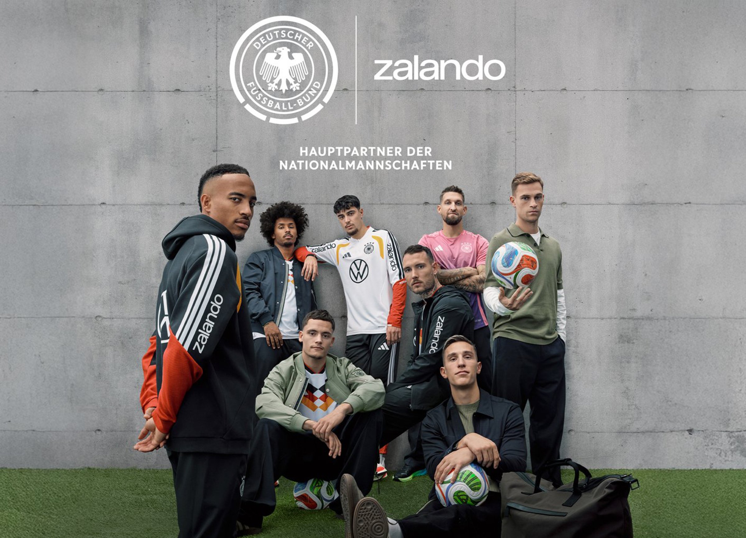 Grupa sportowców w codziennym odzież sportowej w różnych kolorach i wzorach, w tym bluzy z kapturem, kurtki i piłki nożne, na tle betonowym.