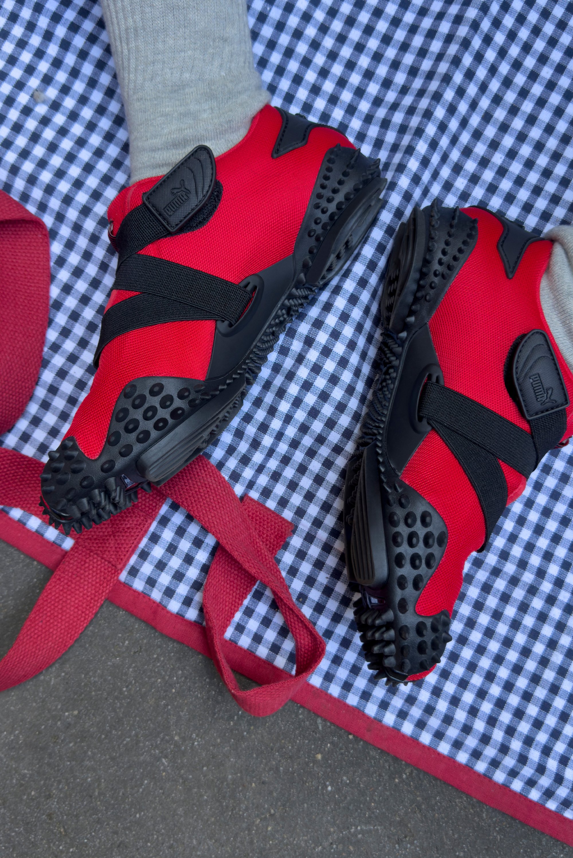 Zapatillas deportivas rojas y negras con suela de goma texturizada y correas de Velcro, exhibidas sobre un fondo de tejido a cuadros.