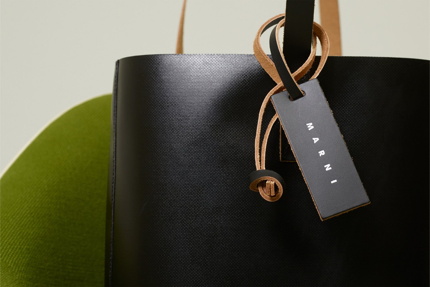 Bolso tote negro de cuero con un acabado texturizado, que presenta una correa de cuero marrón y una etiqueta rectangular grabada con "MARNI."