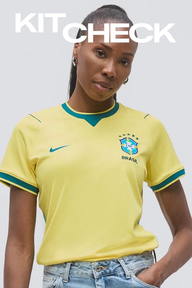 Femeie purtând un tricou galben de fotbal al Braziliei, cu margini albastre și verzi, stând cu o mână în buzunarul blugilor, pe un fundal simplu.