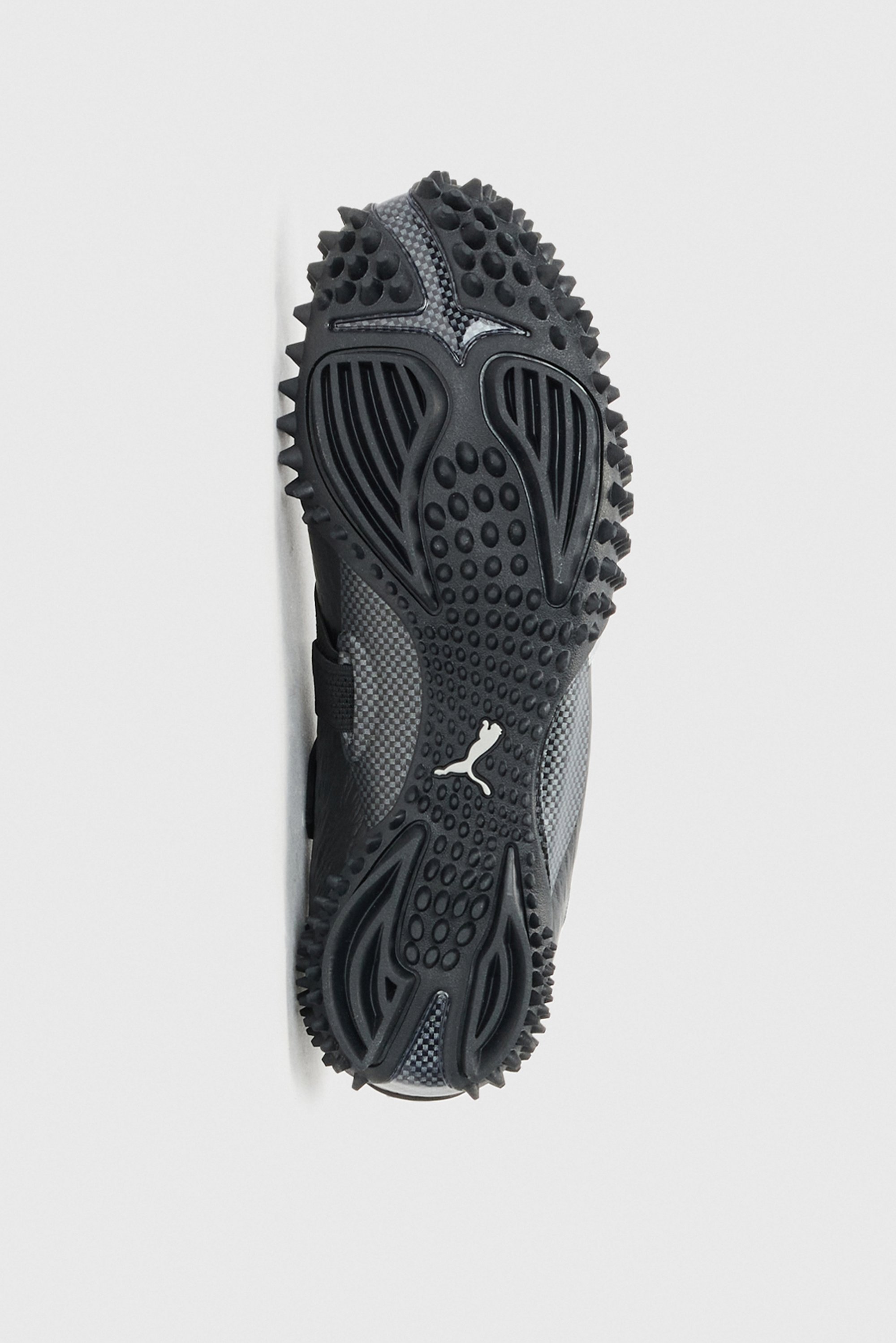Suela de zapatilla deportiva negra con dibujo de goma texturizada, que presenta estrías curvas y clavos circulares para ofrecer tracción. Diseño sencillo y funcional.