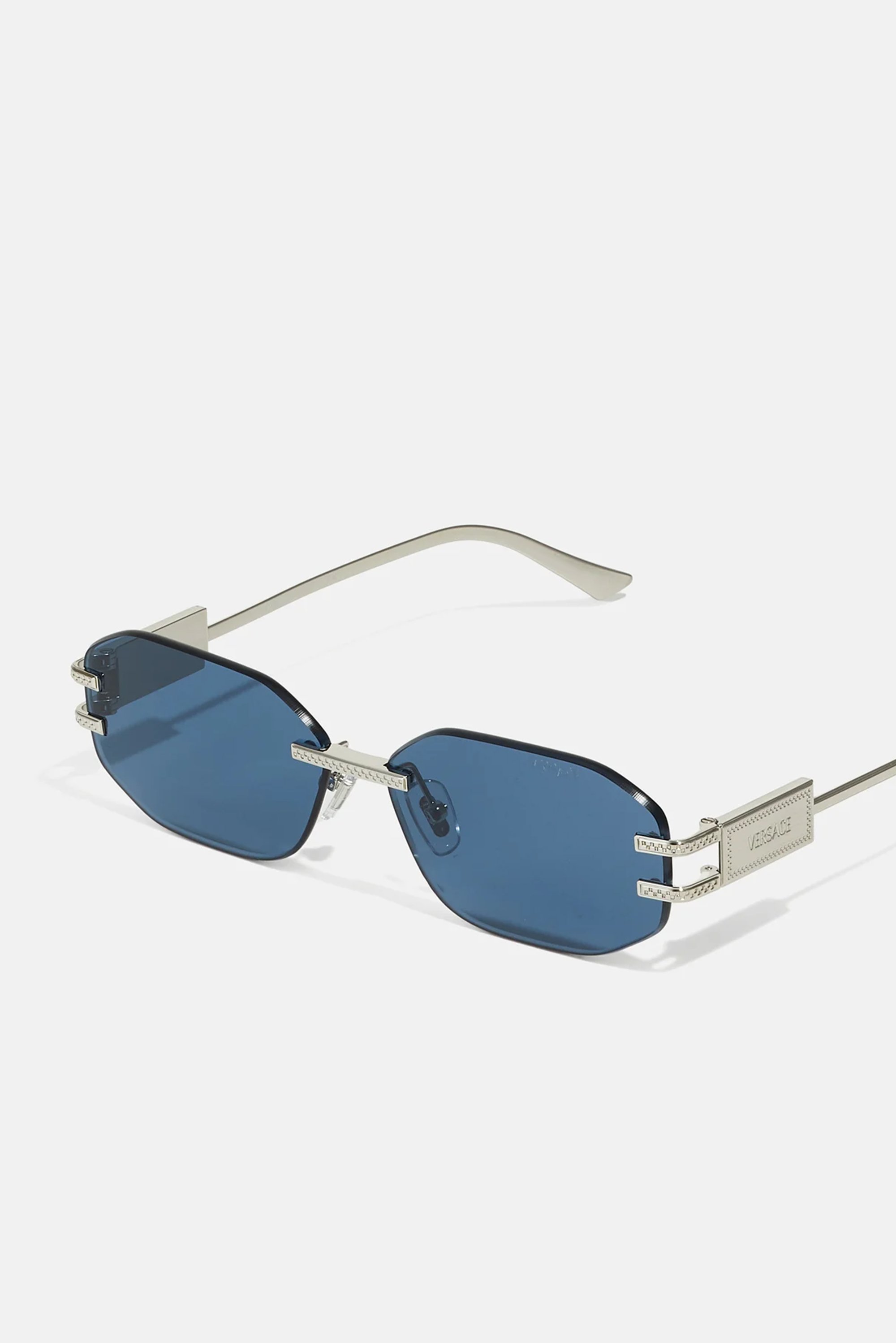 Gafas de sol con tinte azul, de forma octagonal, con detalles en metal plateado y una patilla texturizada. Presenta un detalle del logotipo en un lado.