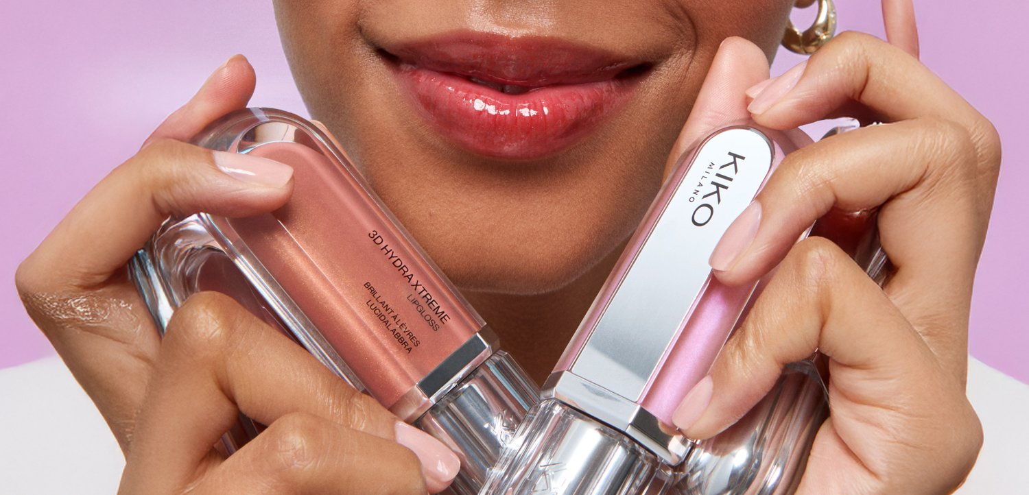 Close-up of lips with glossy pink lipstick, holding two lip gloss tubes, one labeled KIKO Milano and the other 3D Hydra Xtreme.