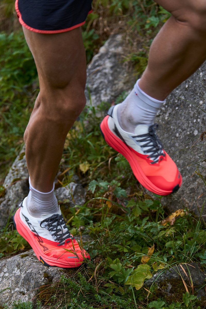 Sports shoes with a white upper and vibrant neon pink front. They feature grey laces, a thick sole, and a rugged tread, designed for outdoor terrain.