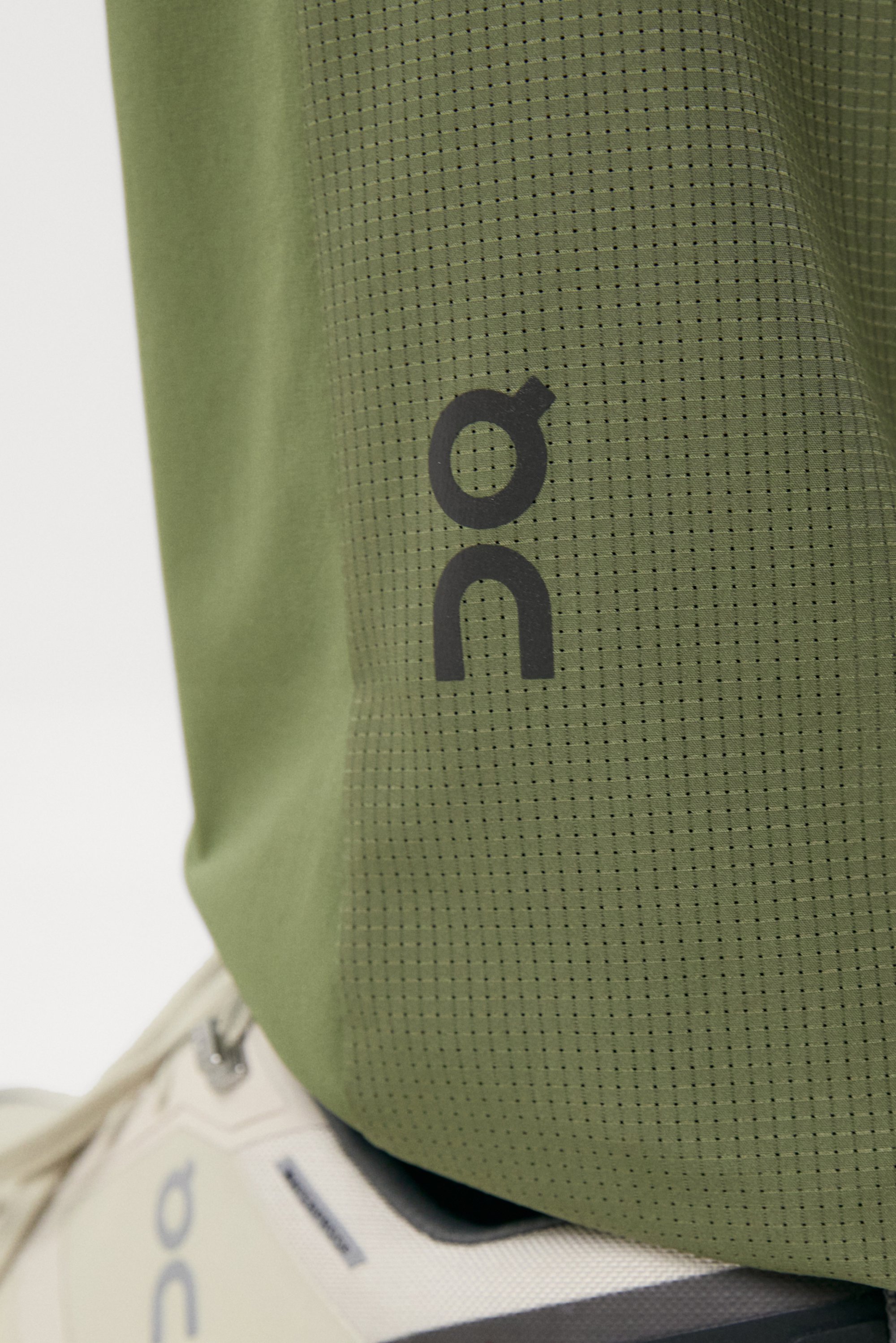 Close-up of a green athletic shirt featuring a logo and a textured pattern, paired with a light-colored running shoe.