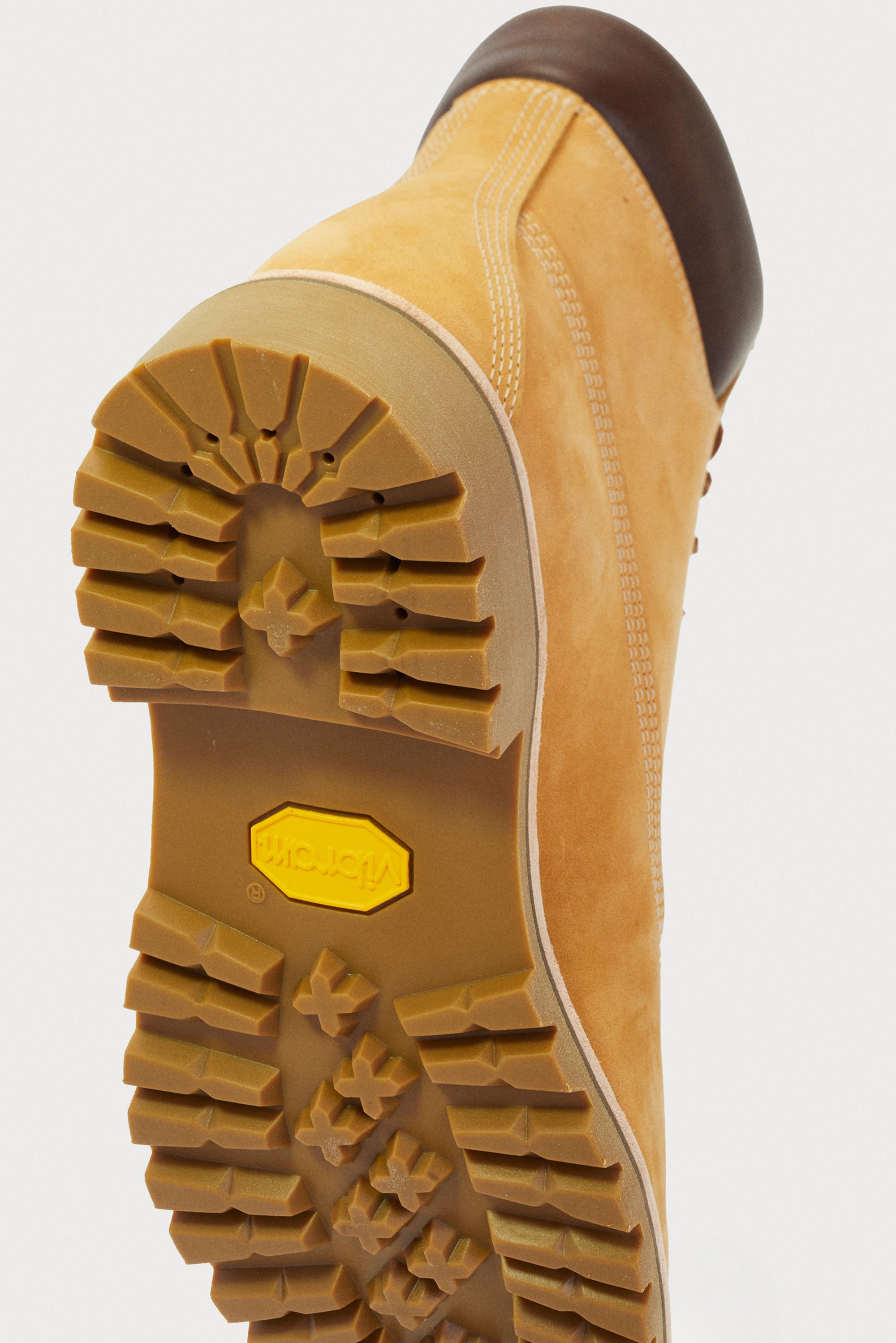 Yellow suede hiking boot with a brown leather cap toe and a rugged rubber sole featuring deep treads for traction. Vibram branding visible.