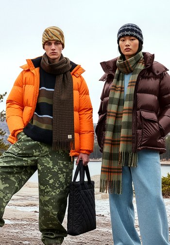 Πορτοκαλί μπουφάν παχυφόρμας, καφέ γυαλιστερό μπουφάν παχυφόρμας, μαντίλια με σχέδια, παντελόνια καμουφλάζ και μαύρη καπιτονέ τσάντα τοτ. Εξωτερικός χώρος, ουδέτερα χρώματα.
