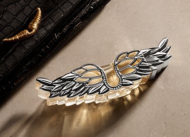 A stylish perfume bottle with wing-shaped embellishments, placed on a textured surface beside a black leather wallet.