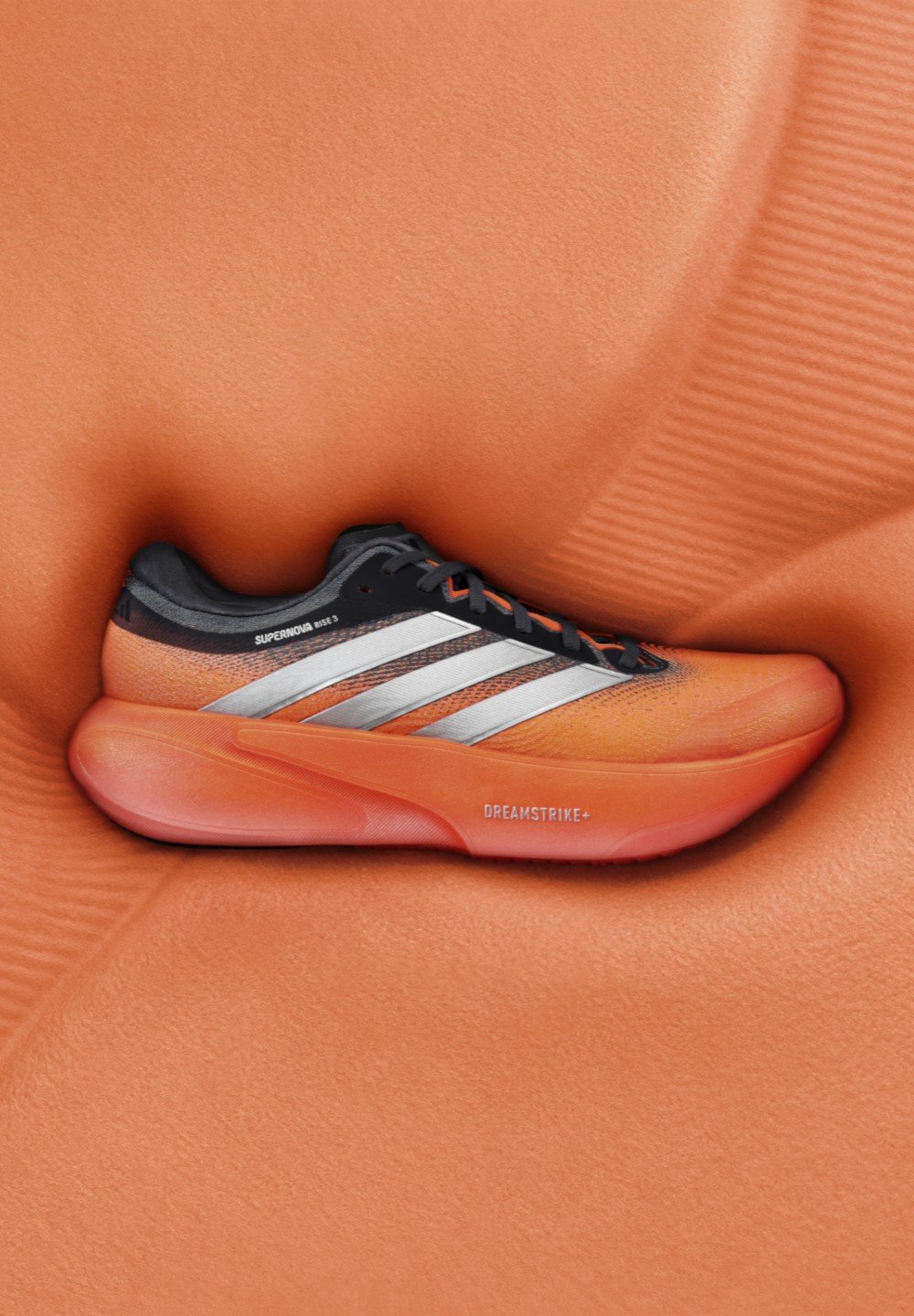 Chaussure de sport orange avec des accents noirs, des bandes argentées et une tige texturée. Présente une semelle extérieure épaisse et arrondie avec le logo "DREAMSTRIKE+".