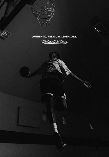 Un joueur s'élance vers un panier de basket avec un ballon à la main, montrant action et athlétisme dans un espace faiblement éclairé. Le texte au-dessus lit "AUTHENTIQUE. PREMIUM. LÉGENDAIRE."