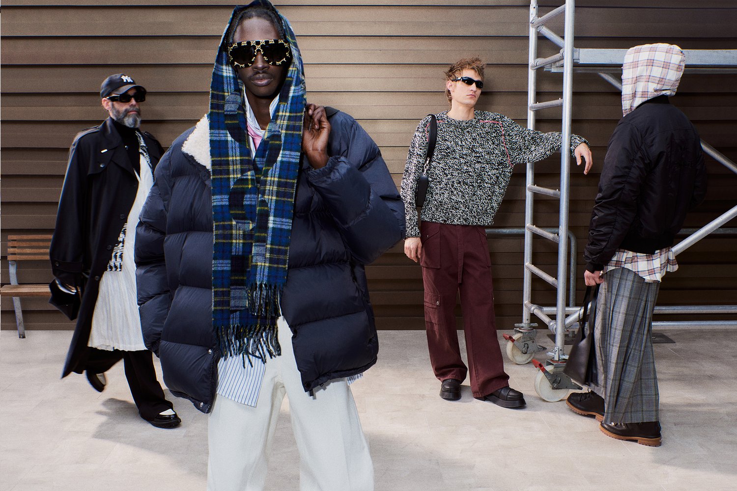 Four individuals showcase diverse fashion styles in an urban setting, featuring a mix of oversized outerwear, unique accessories, and casual attire.