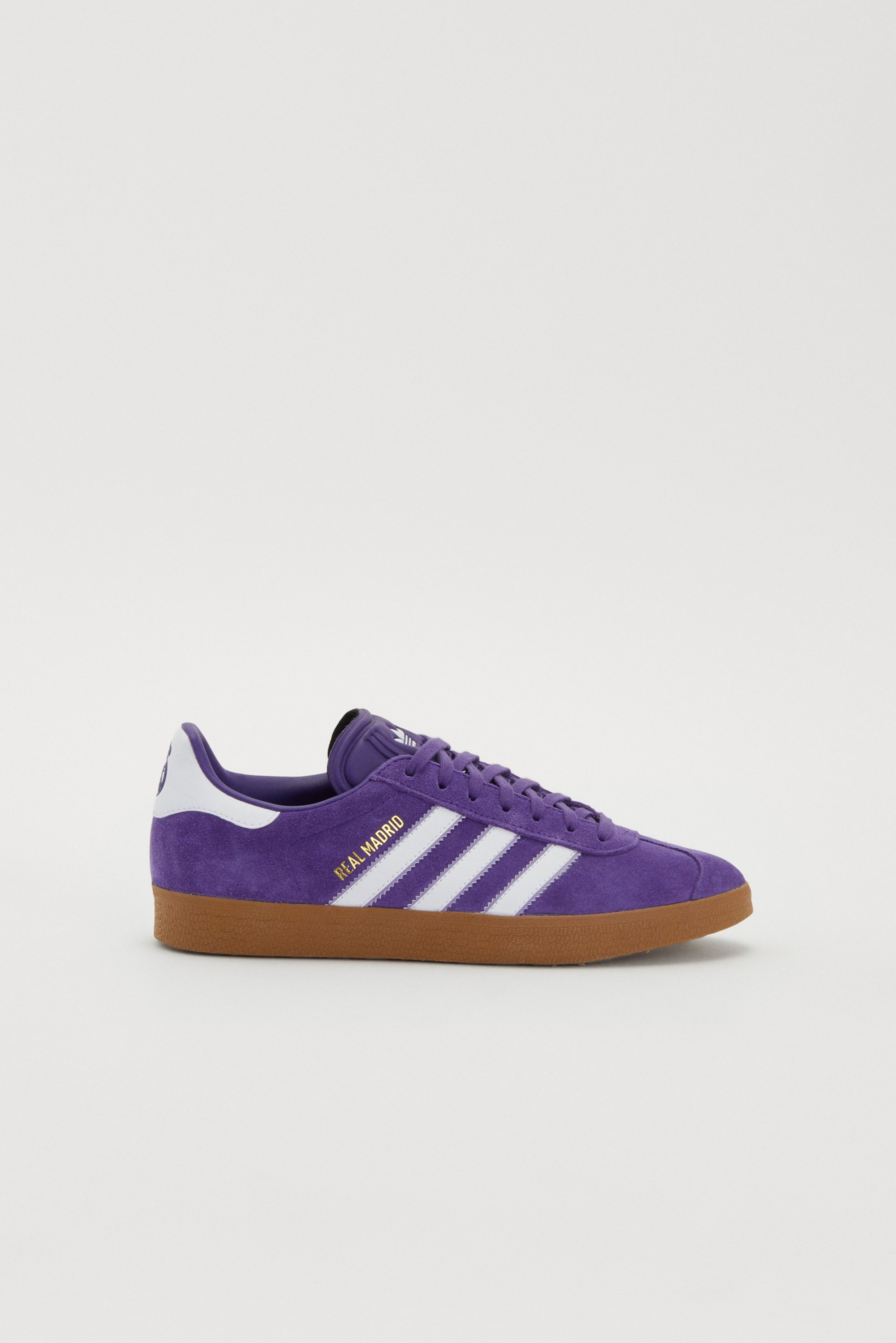 Paarse Adidas sneakers met witte strepen en een gumzool, met "R.E.A.L. MADRID" gedrukt op de zijkant.