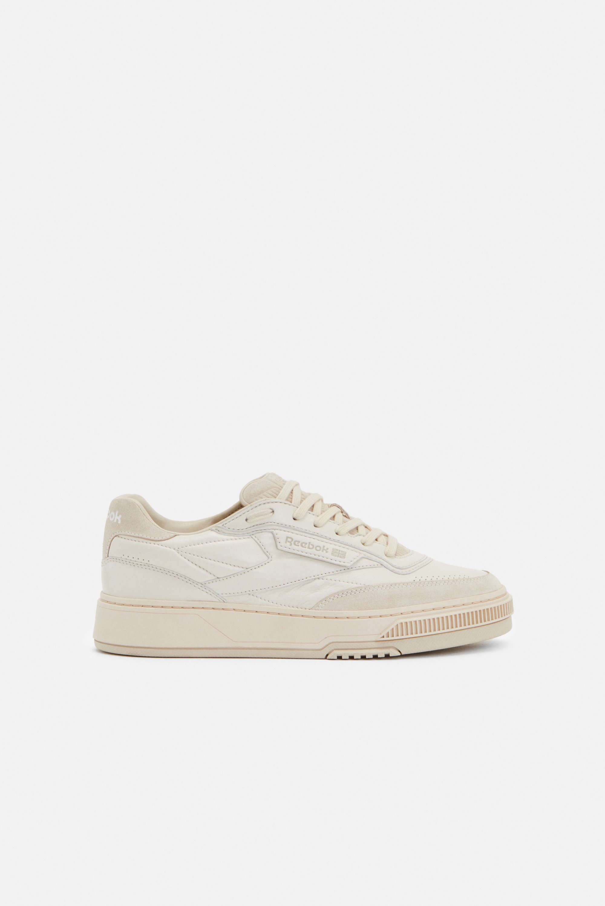 Zapatillas Reebok beige con cuero texturizado y ante, que presentan una suela gruesa, puntera redonda y un sistema de cordones prominente.