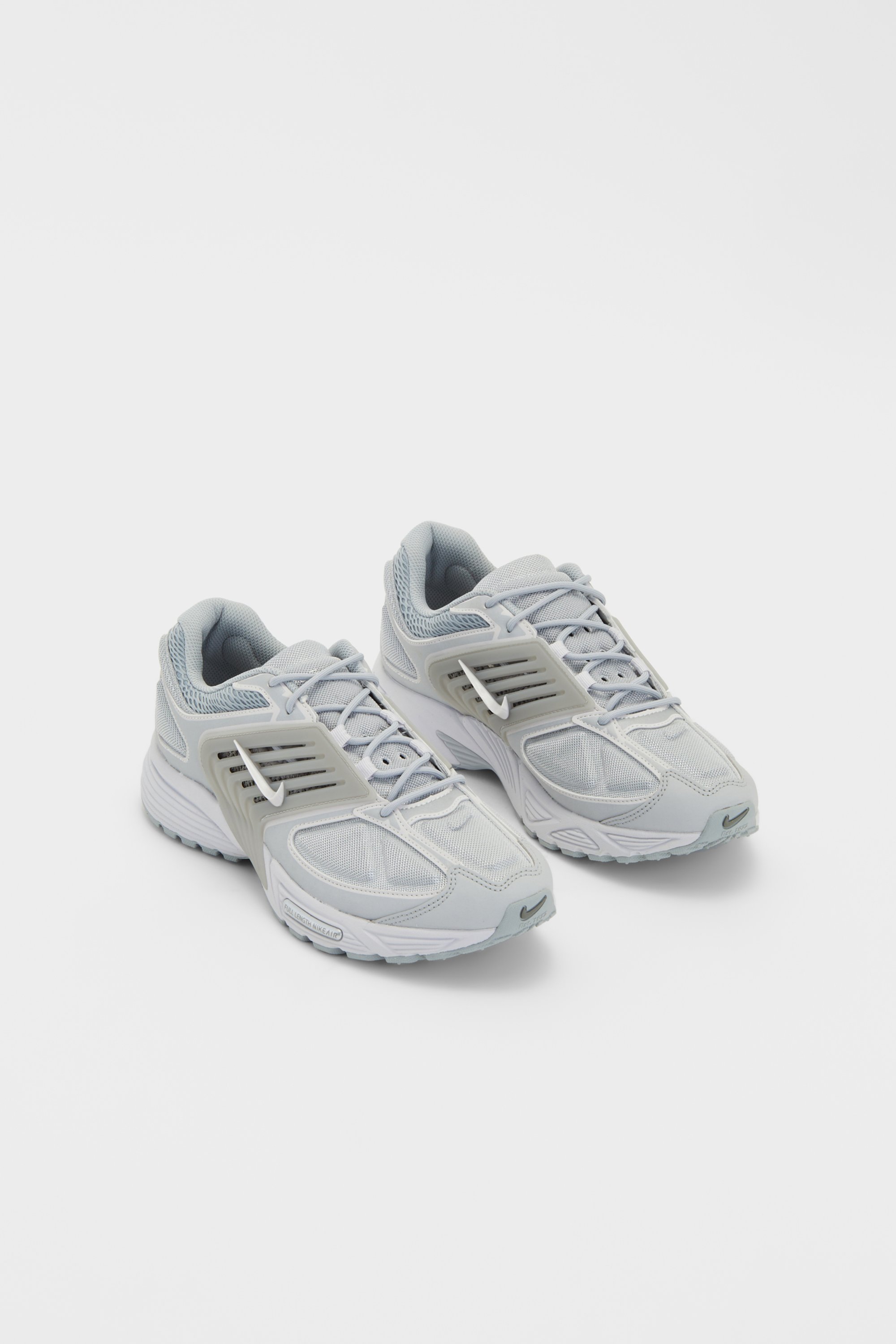 Light gray athletic shoes with mesh detailing and a white Nike swoosh, placed side by side on a white background.