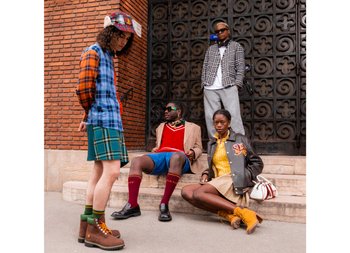 Four stylish individuals in colorful outfits pose on steps against a brick wall, showcasing diverse fashion choices and modern accessories.