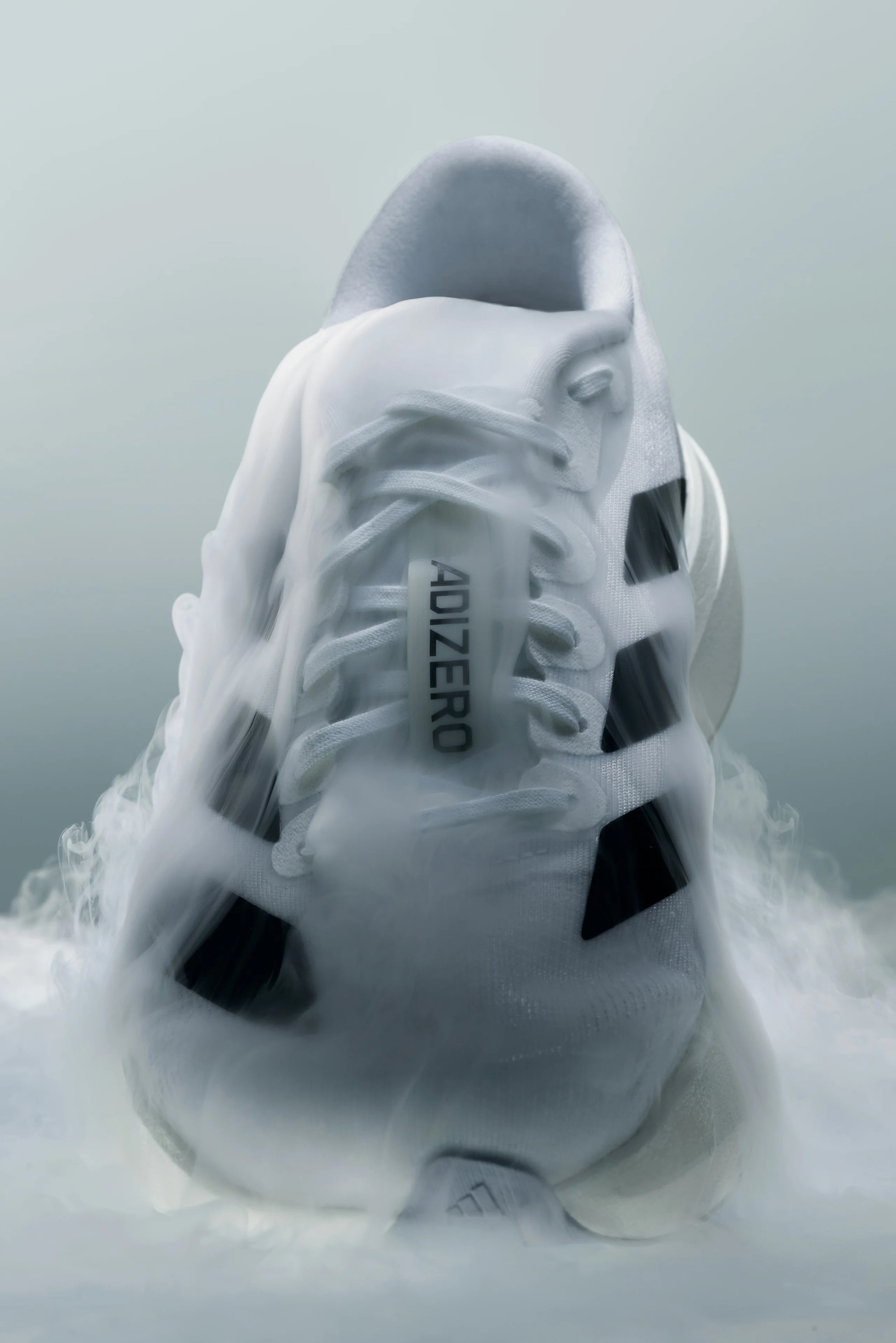 Un primer plano de una zapatilla deportiva blanca con la marca "ADIZERO", parcialmente envuelta en niebla, destacando su diseño elegante y detalles.