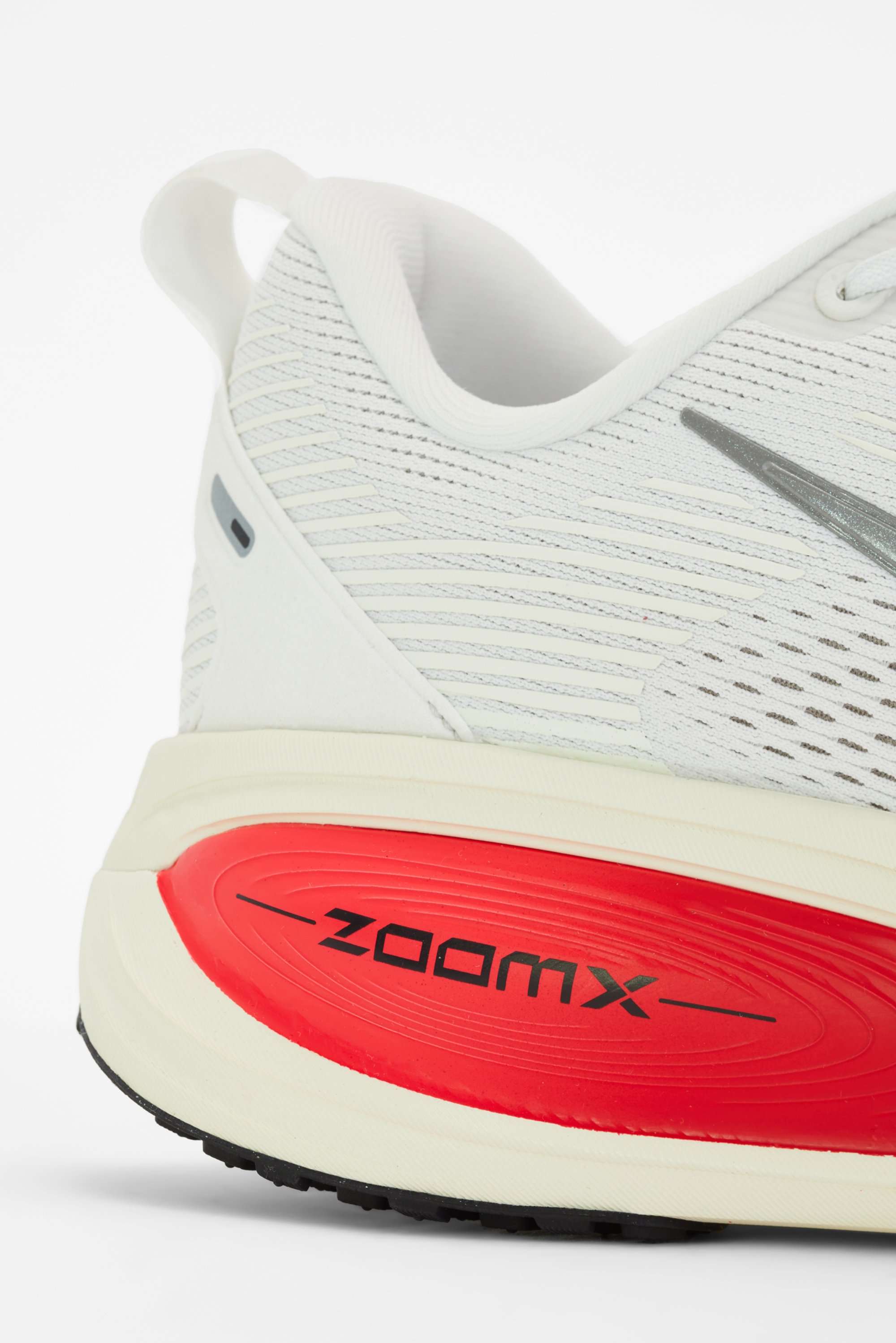 Primer plano de una zapatilla deportiva blanca que destaca un upper texturizado y una suela de amortiguación roja prominente etiquetada como "ZOOMX."